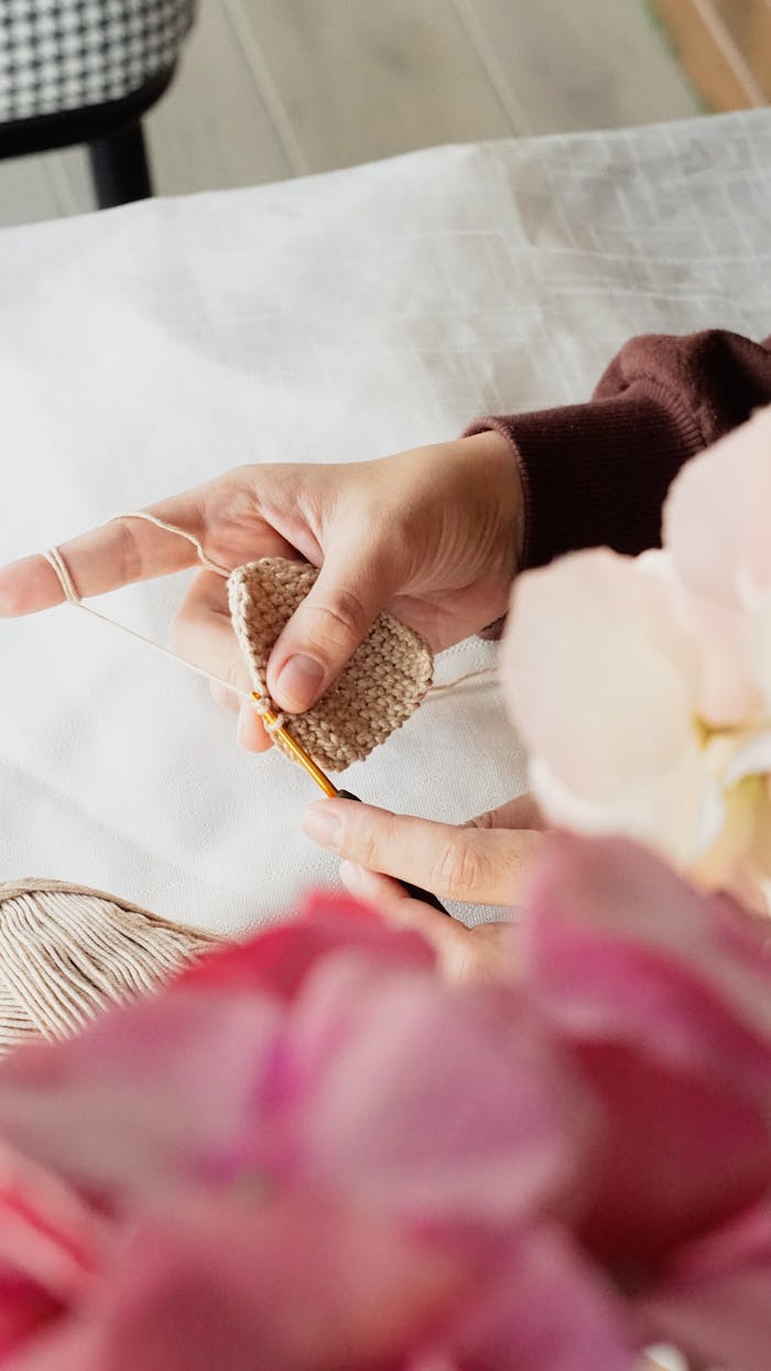 Detailed view of a person's hands crocheting with a soft yarn and crochet needle, invoking creativity and craftsmanship.